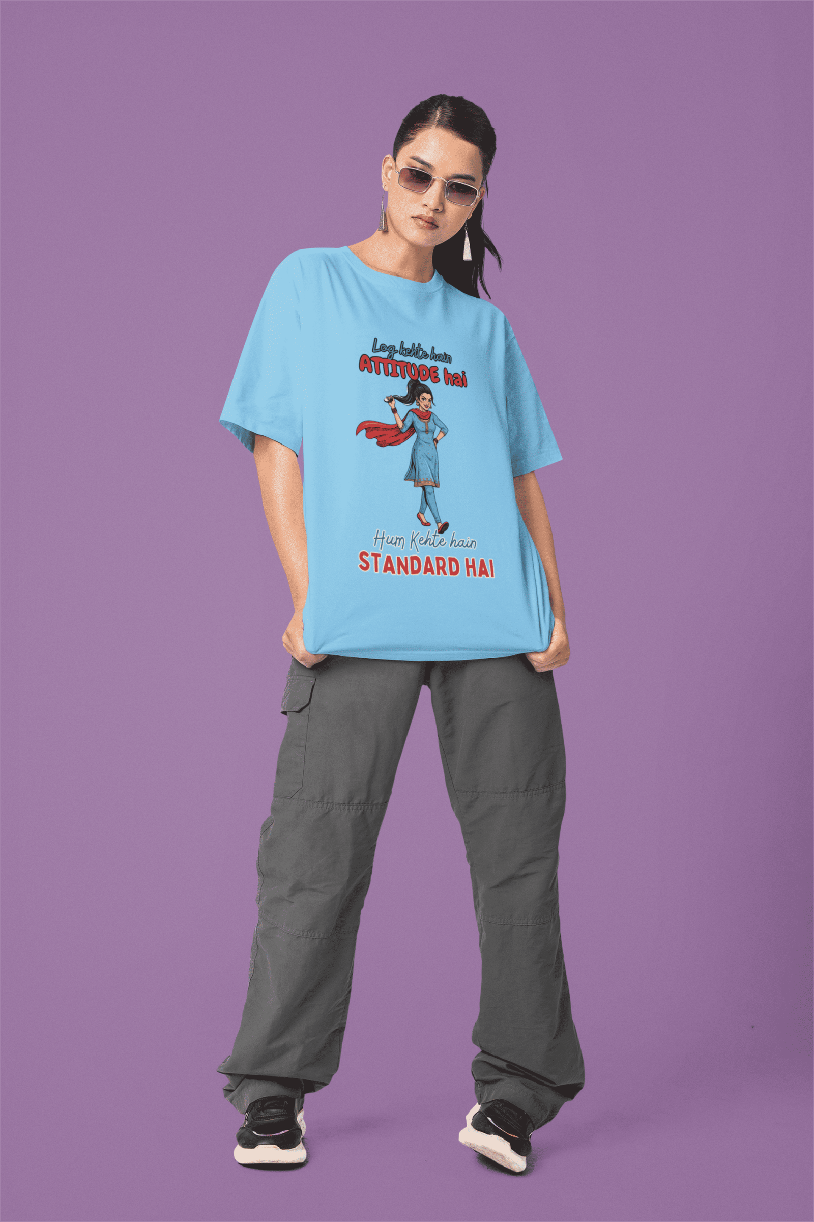 Baby Blue Desi Swag Oversized Tee by PodLyft. A model wearing sunglasses poses in a light blue oversized t-shirt with a funny "Attitude vs Standard" graphic print.