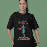 Black Desi Swag Oversized Tee by PodLyft. A model wears a black t-shirt featuring a confident Desi girl illustration and the Hindi text "Log kehte hain ATTITUDE hai, Hum Kehte hain STANDARD HAI."